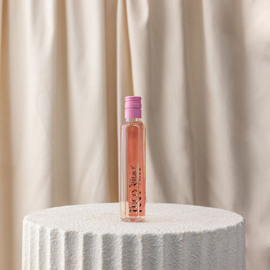 Pink bottle with a pink cap on a white pedestal against a beige curtain background