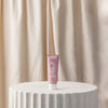 Pink tube of toothpaste on a textured white surface with a beige curtain background