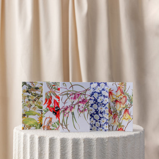 Five floral greeting cards on a textured surface with a beige curtain background