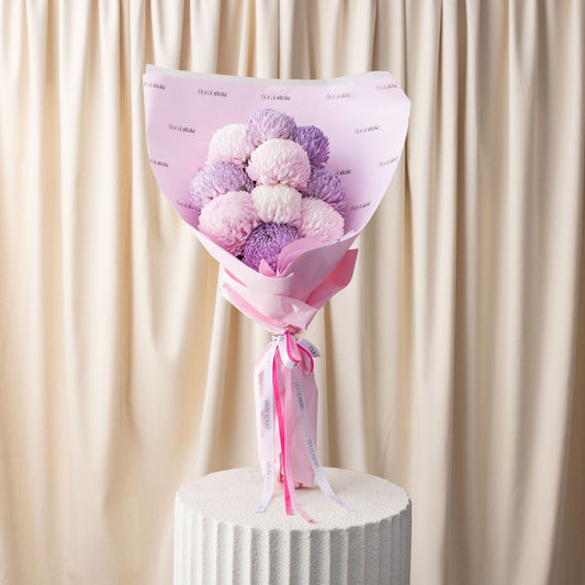 Bouquet of pink and purple pom-poms with a pink paper wrap on a beige curtain background