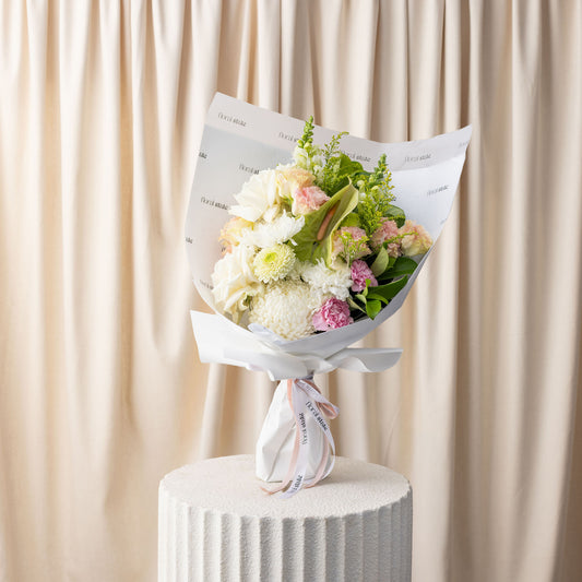 Bouquet of flowers wrapped in paper on a white pedestal with a beige curtain background