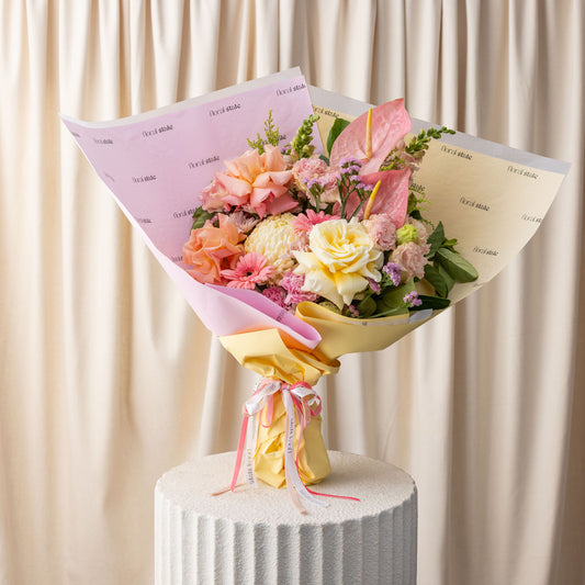 Bouquet of flowers wrapped in pink and yellow paper on a white pedestal with a beige curtain background