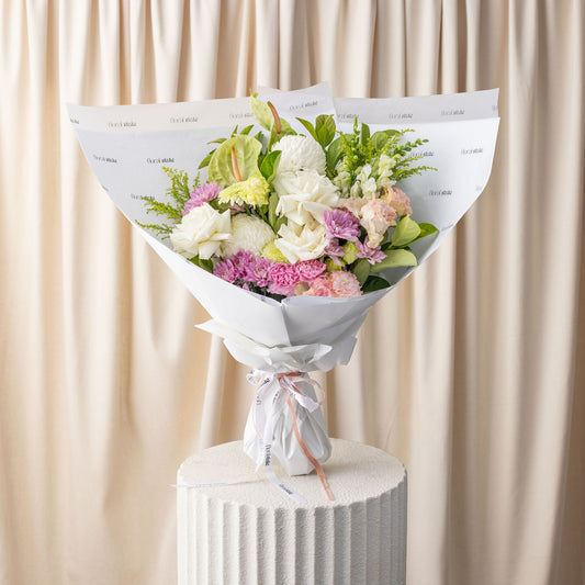 Bouquet of flowers wrapped in white paper on a cylindrical white stand with a beige curtain background