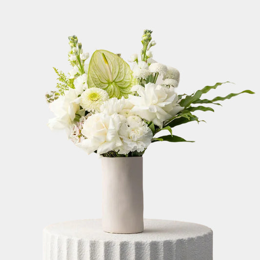 Floral arrangement with white flowers and a green leaf in a white vase on a light gray background