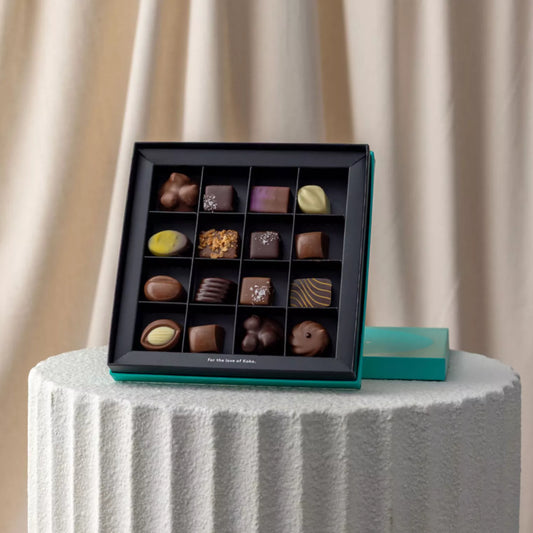 Assorted chocolates in a black box on a white pedestal with a beige curtain background