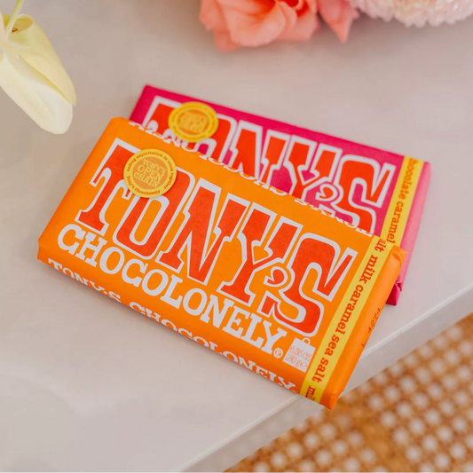 Two Tony's Chocolonely chocolate bars on a white surface with flowers in the background.
